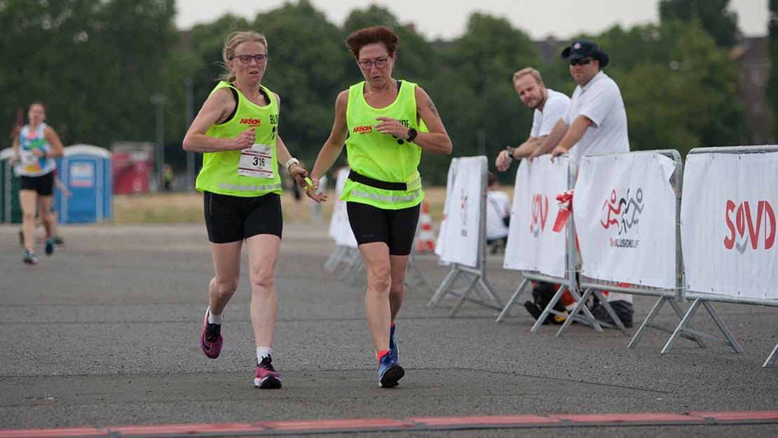 Zwei Frauen (blind und Guide) überqueren die Ziellinie beim SoVD-Inklusionslauf